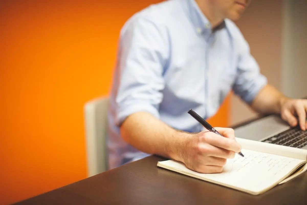 office-employee-with-laptop-writing-on-notepad-with-pen