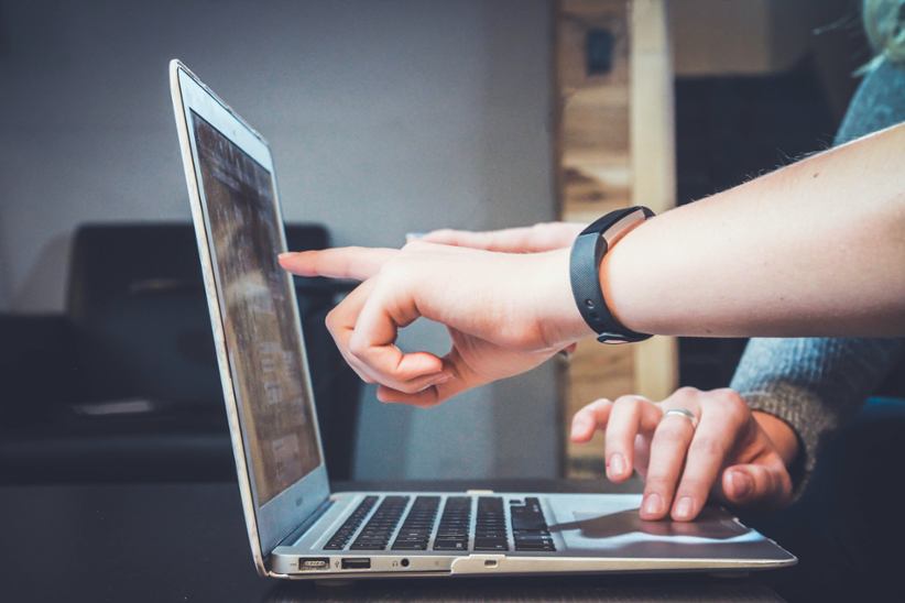 A computer and two people discussing something.