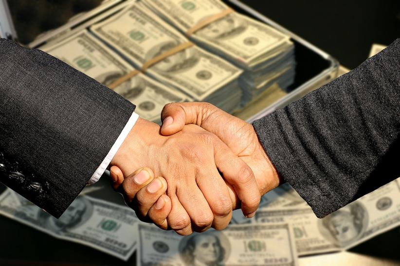 businessmen-shaking-hands-money-in-background