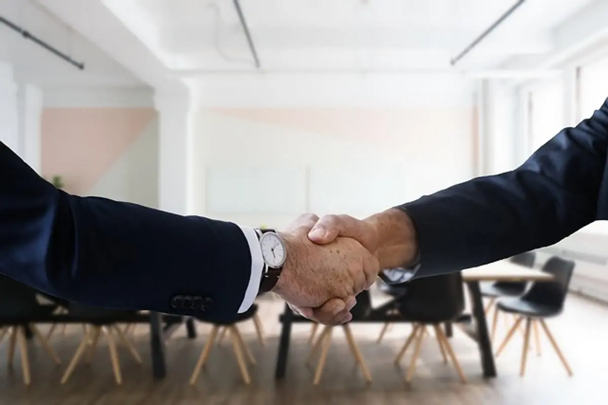 two-businessmen-shake-hands-office-in-background