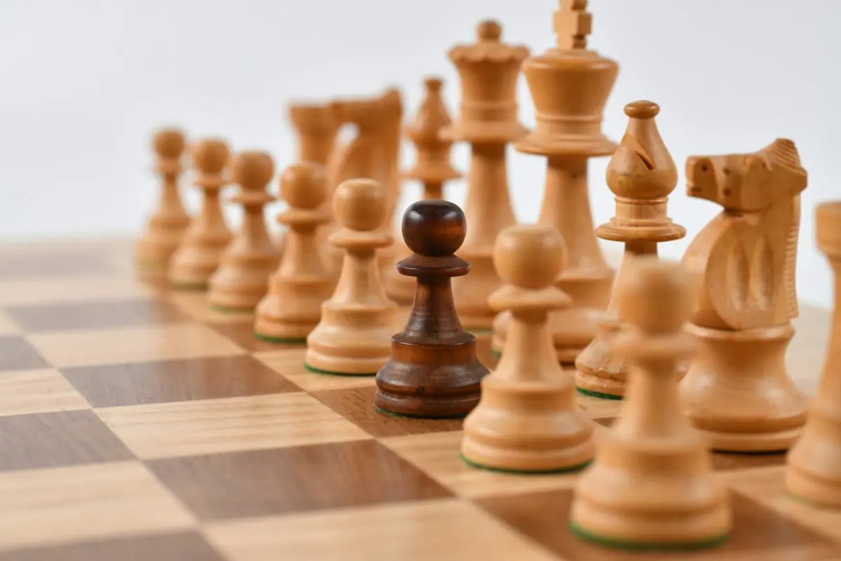 A black pawn amid white chess pieces.